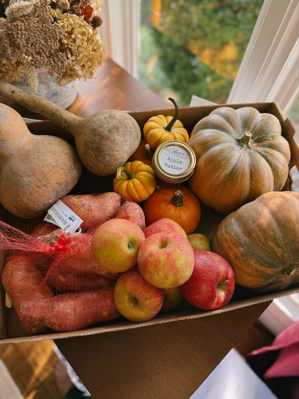 Box of seasonal local produce including squash, apples, and apple butter