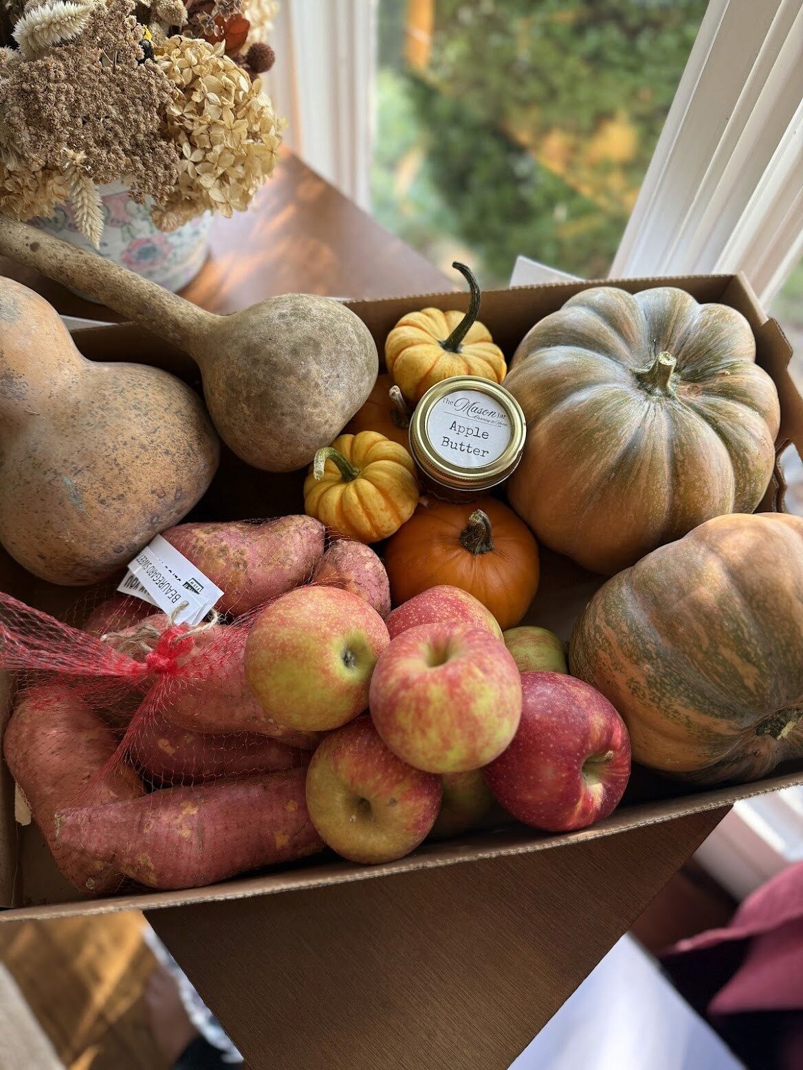 Box of seasonal local produce including squash, apples, and apple butter